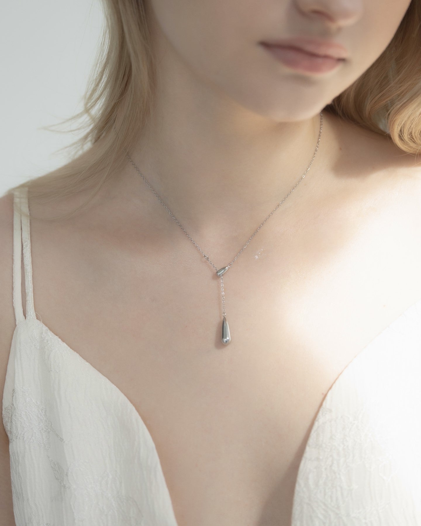 ドロップトップネックレスを着用した女性の首元のクローズアップ。シンプルで優雅なドロップ型デザインが特徴のステンレス製ネックレス。