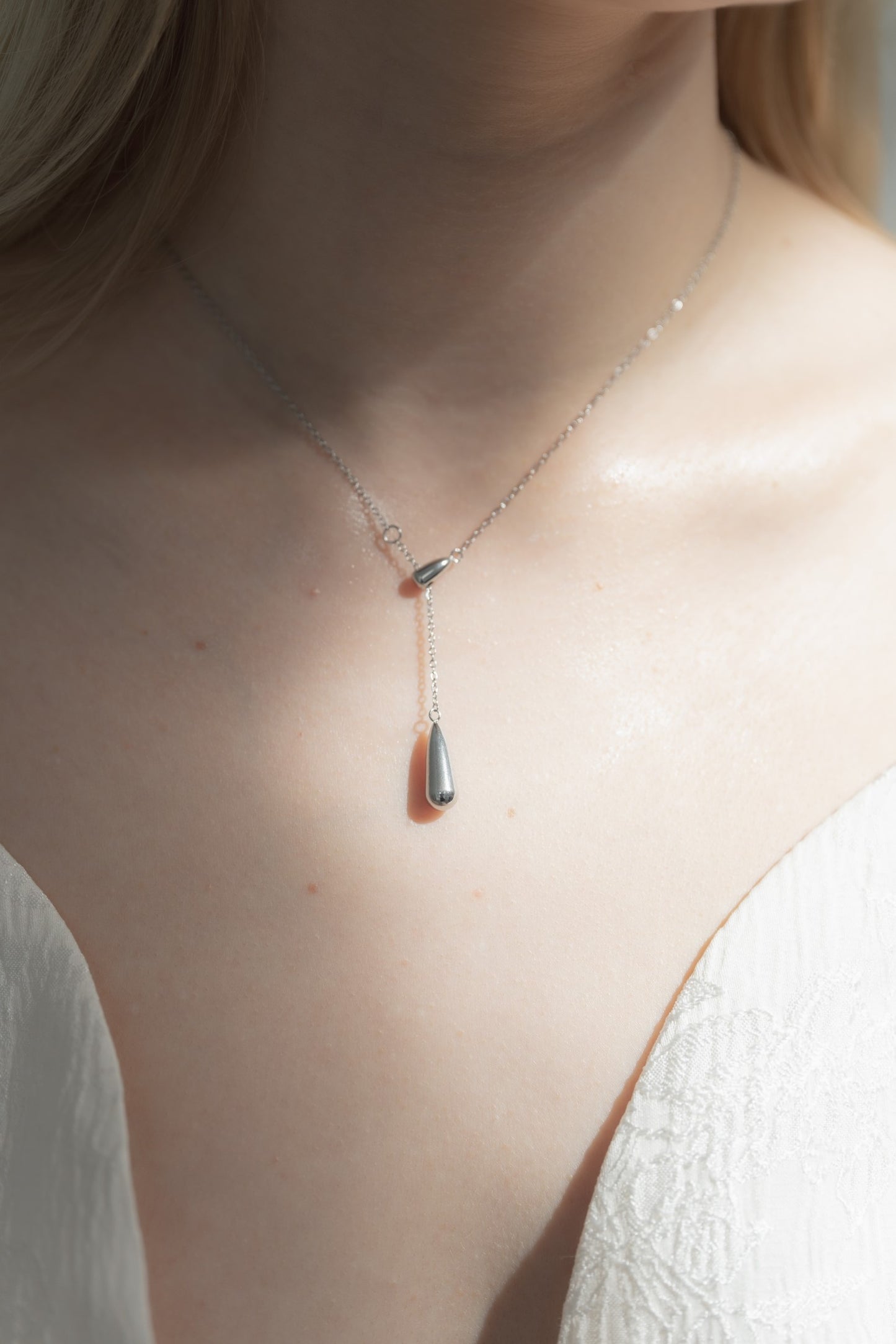 ドロップトップネックレスを着用した女性の首元のクローズアップ。シンプルで優雅なドロップ型デザインが特徴のステンレス製ネックレス。