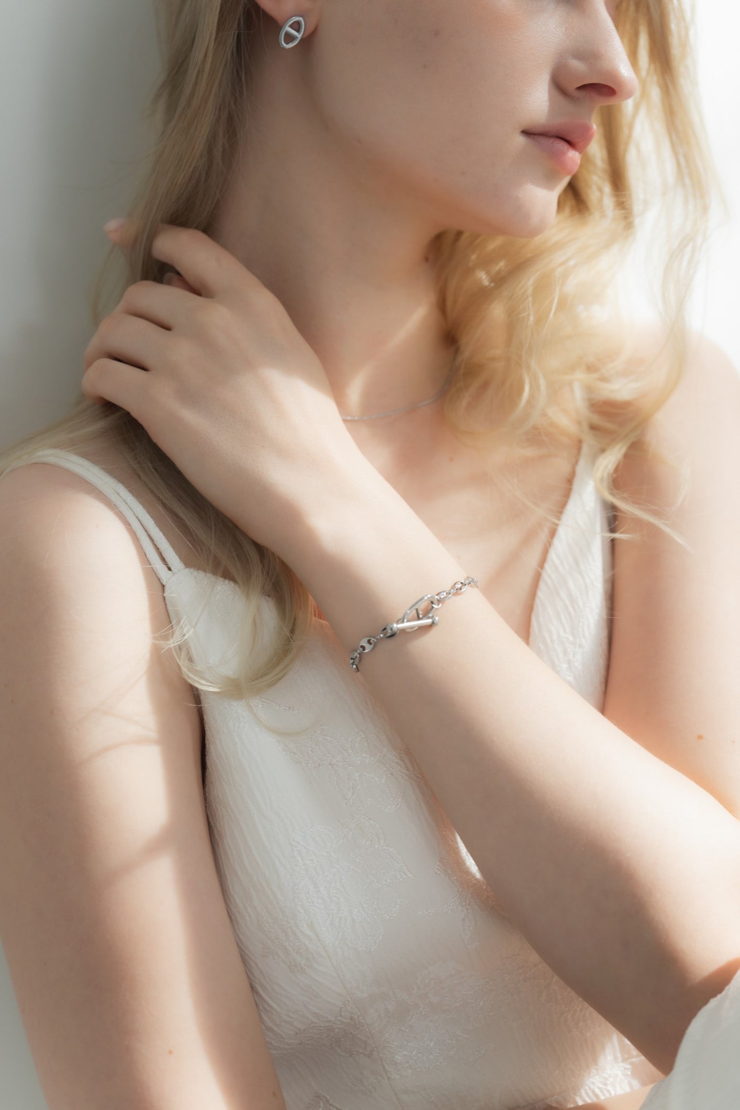 他のジュエリーと一緒にモチーフチェーンブレスレットを着用する女性。重ね付けにも最適で、コーディネートにアクセントを加えるデザイン。