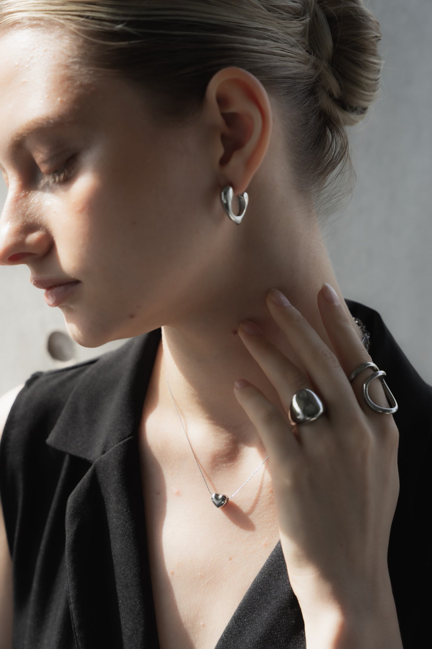 他のジュエリーと一緒にハートピースを着用する女性。シンプルで洗練されたデザインが、他のアクセサリーとも調和し、重ね付けにも最適。