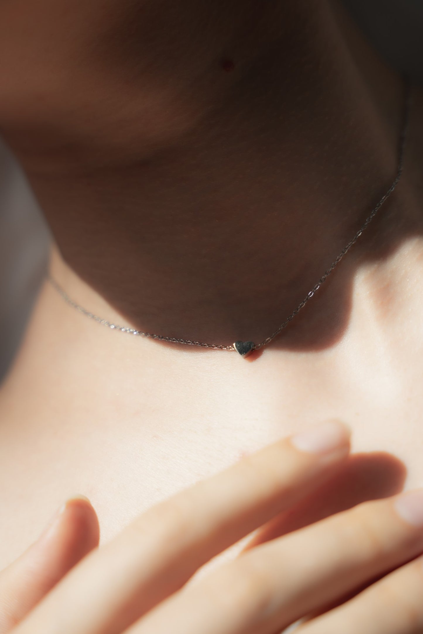 日常使いとしてミニハートネックレスを着用する女性。軽量で快適に着用できる、フェミニンで愛らしいデザインのネックレス。