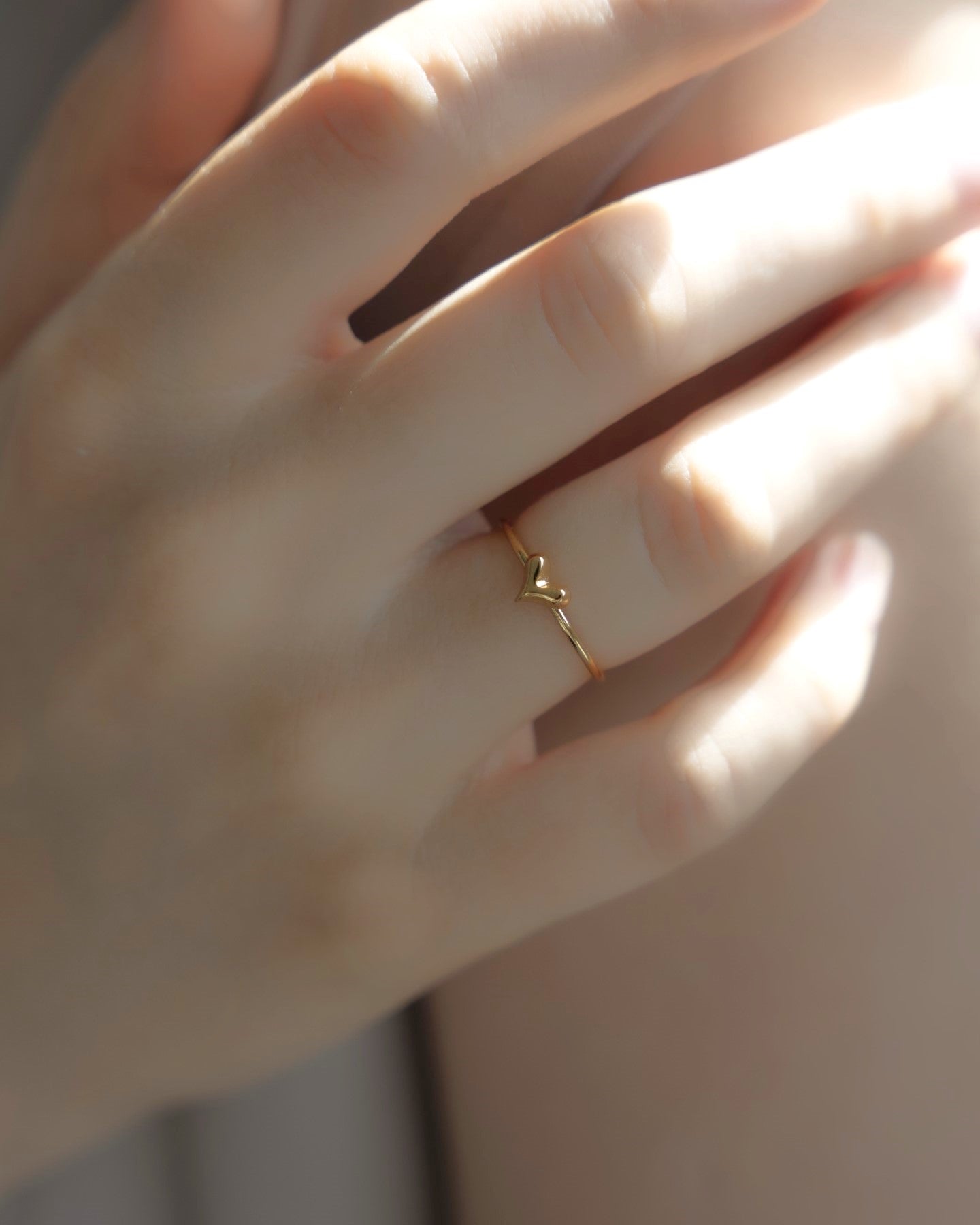 ミニハートリングを着用した女性の手元のクローズアップ。小さく愛らしいハートモチーフが指先を飾るステンレス製リング。