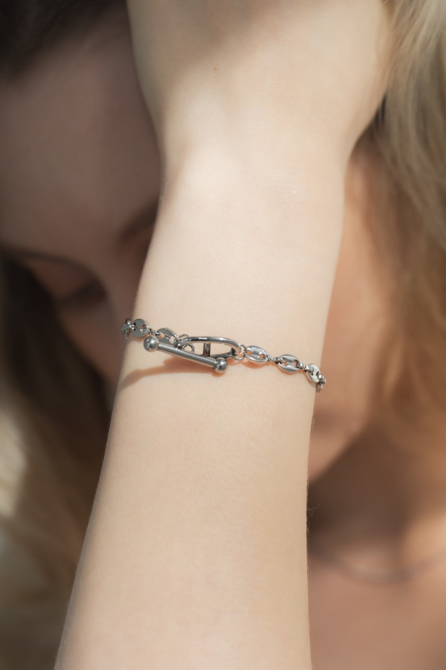 モチーフチェーンブレスレットを着用した女性の手首のクローズアップ。ユニークなモチーフと洗練されたチェーンが特徴のアクセサリー。