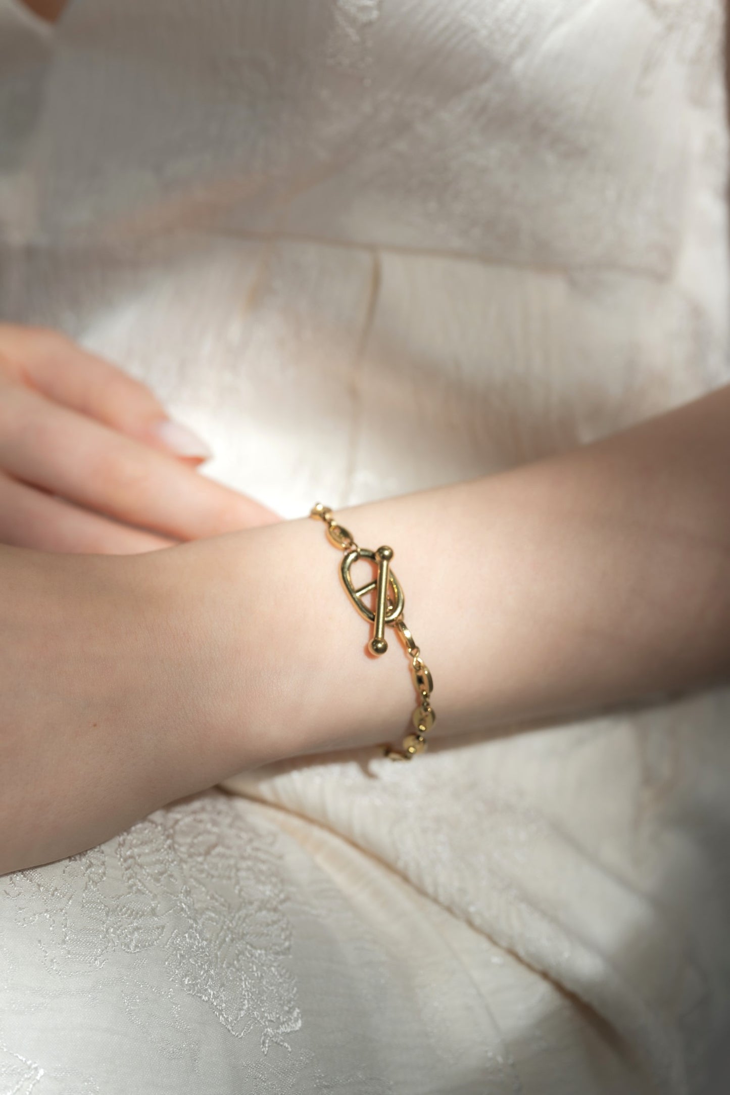 他のジュエリーと一緒にモチーフチェーンブレスレットを着用する女性。重ね付けにも最適で、コーディネートにアクセントを加えるデザイン。