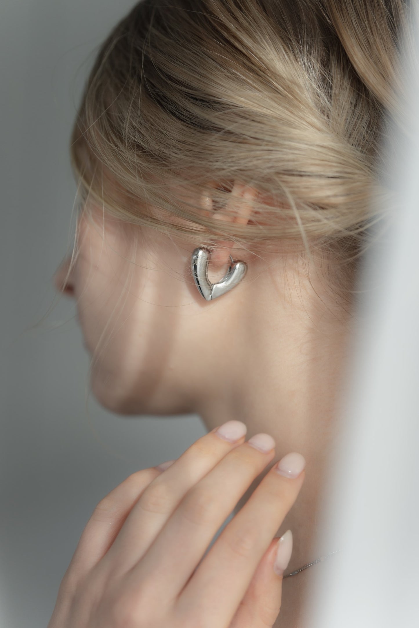 ニュアンスハートフープピアスを着用した女性の耳元のクローズアップ。エレガントで愛らしいハート型のステンレス製ピアス。