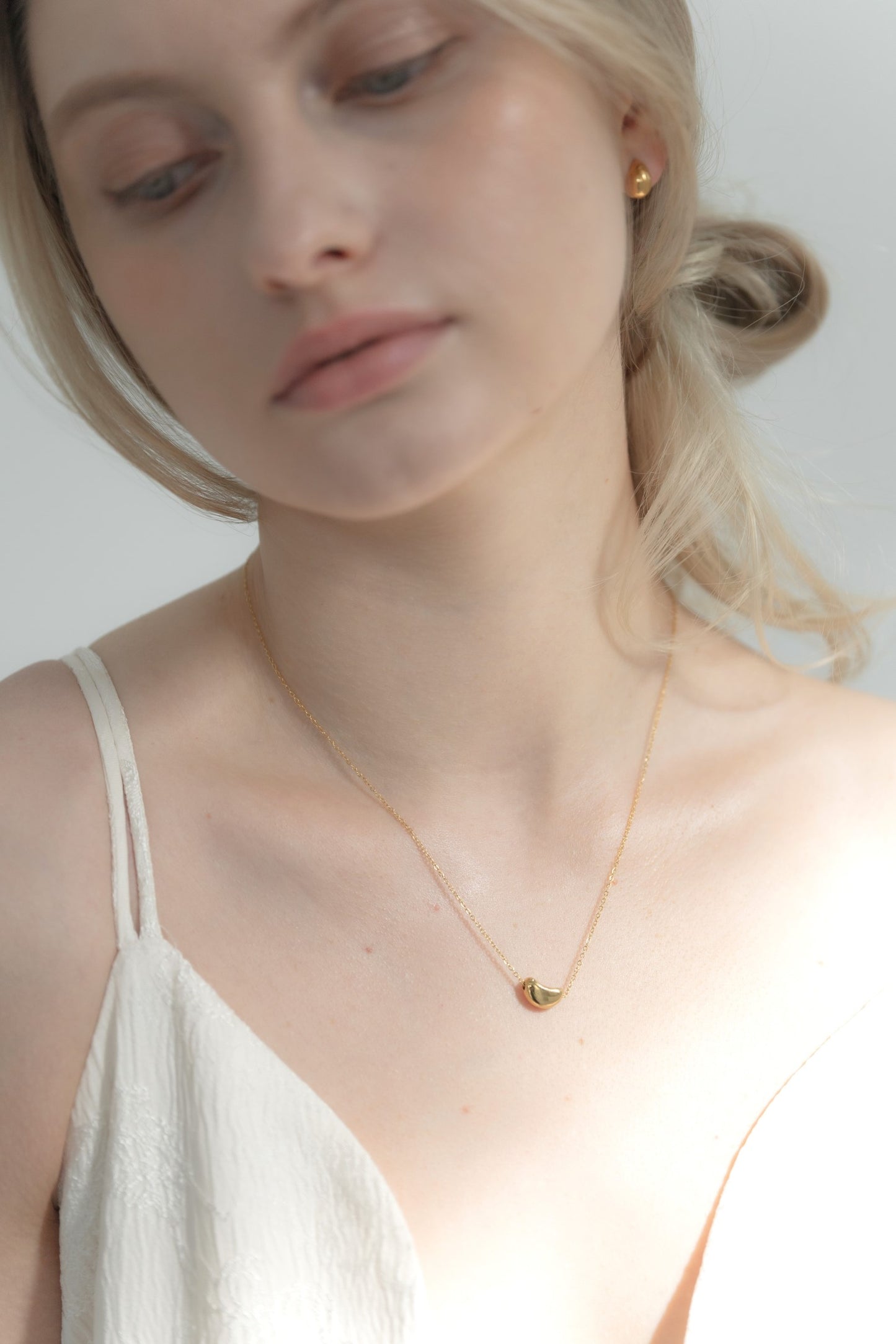 他のジュエリーと一緒にニュアンスハートネックレスを着用する女性。重ね付けスタイルで、上品なコーディネートに最適。