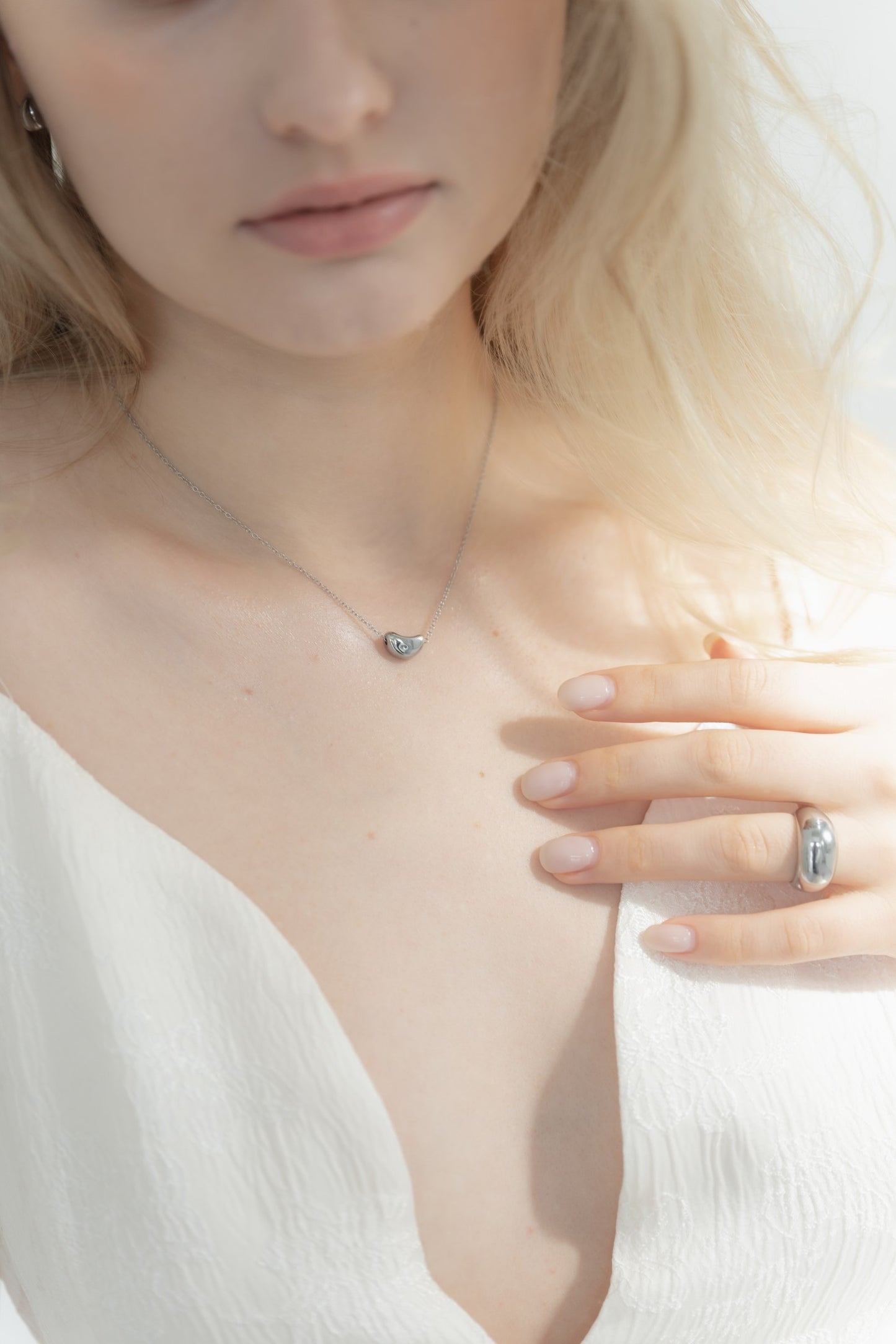 他のジュエリーと一緒にニュアンスハートネックレスを着用する女性。重ね付けスタイルで、上品なコーディネートに最適。