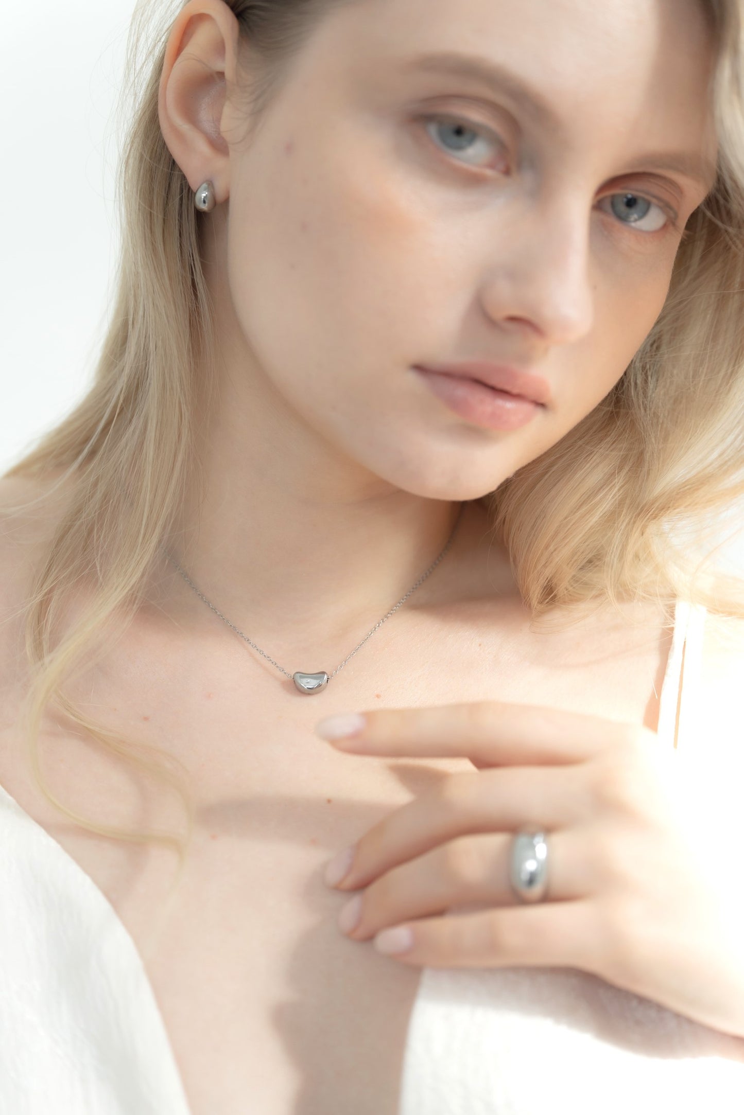 他のジュエリーと一緒にニュアンスハートネックレスを着用する女性。重ね付けスタイルで、上品なコーディネートに最適。