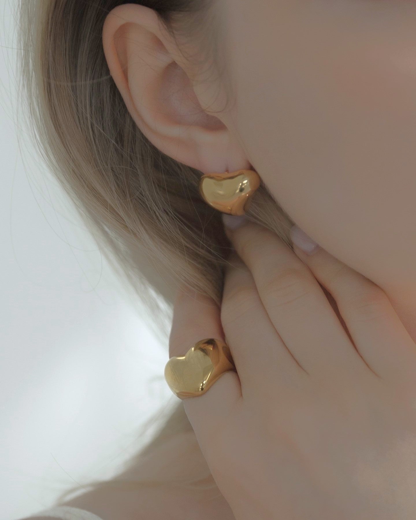 他のジュエリーと一緒にニュアンスハートピースを着用する女性。重ね付けにぴったりなアクセサリー。