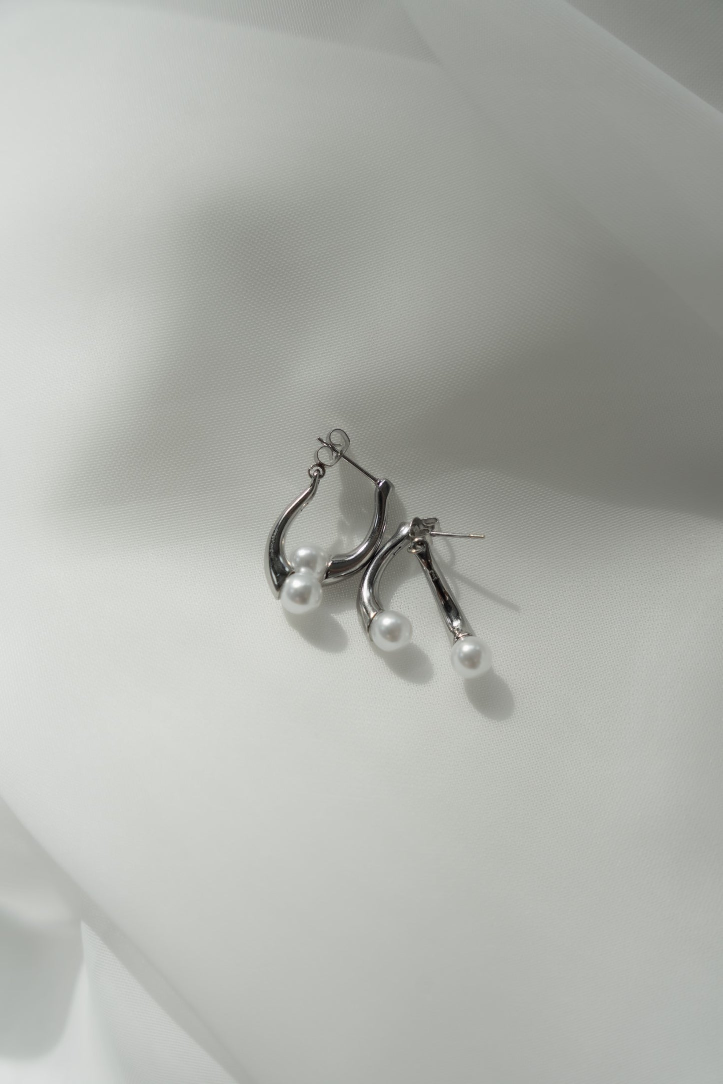 白い背景に置かれたパール×ドロップピアス。シンプルでありながら優雅なパールデザインが際立つアクセサリー。