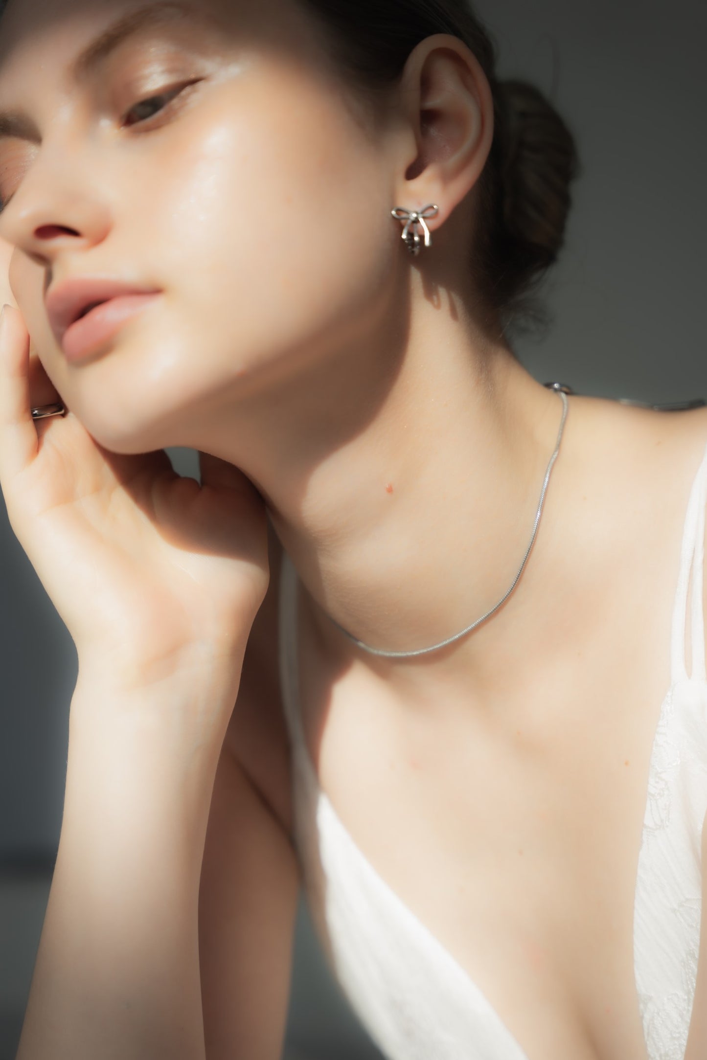 他のジュエリーと一緒にリボンイヤリングを着用する女性。リボンモチーフが他のアクセサリーと調和し、重ね付けにも最適。