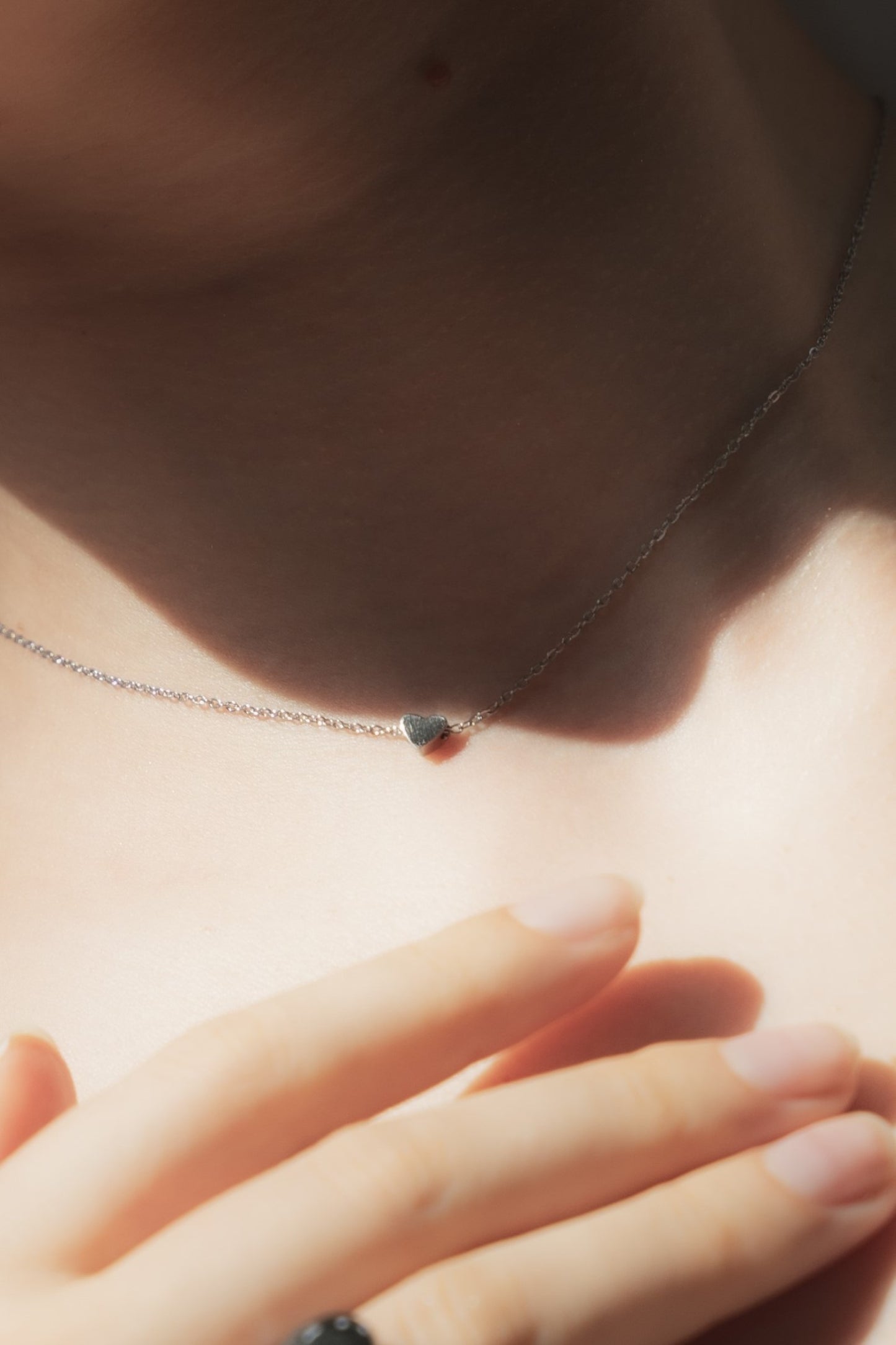 ミニハートネックレスを着用した女性の首元のクローズアップ。シンプルで愛らしいミニサイズのハートが特徴のステンレス製ネックレス。
