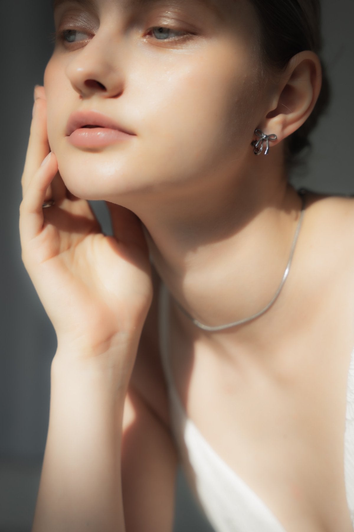 リボンイヤリングを着用した女性の耳元のクローズアップ。フェミニンで愛らしいリボンモチーフが特徴のステンレス製イヤリング。