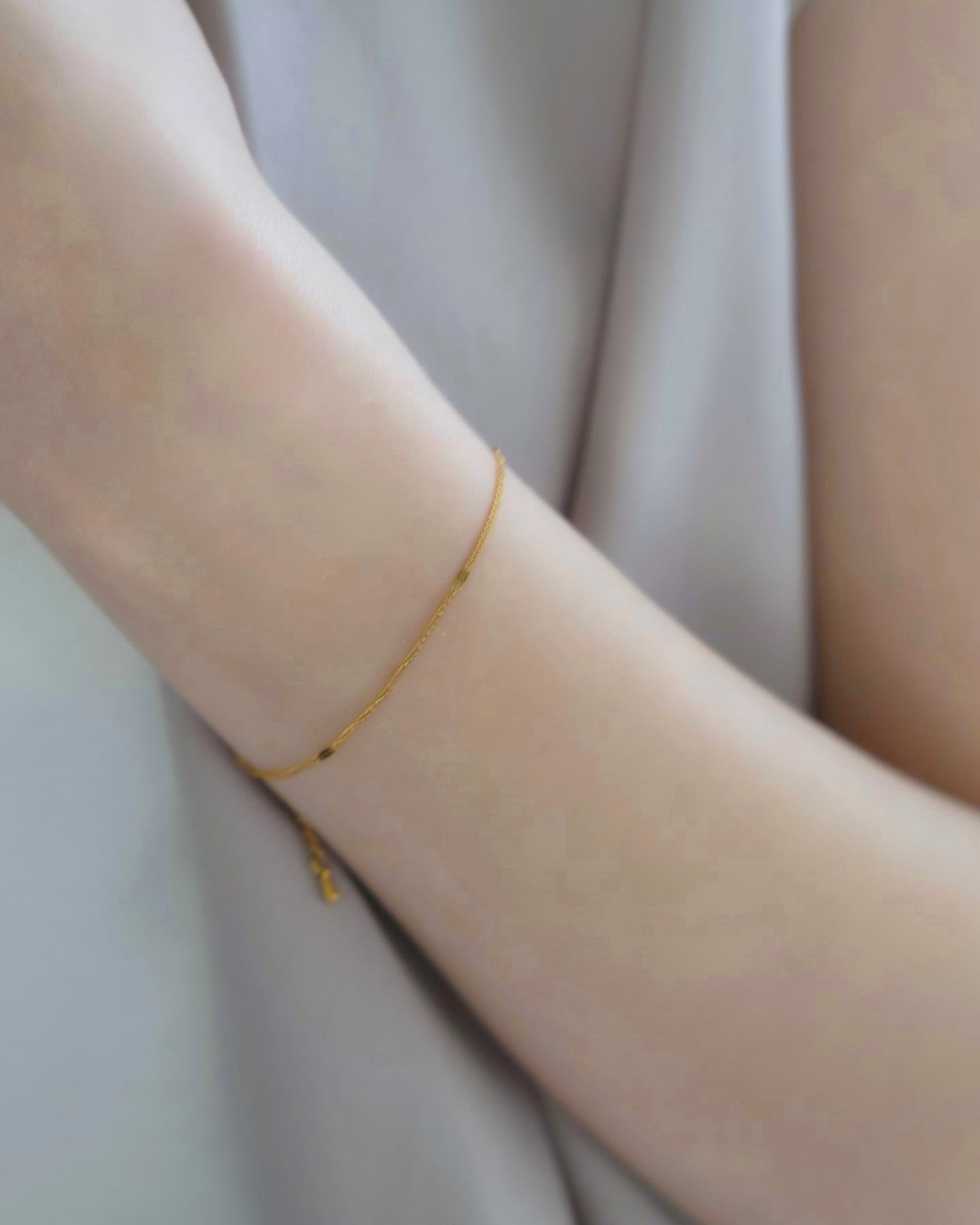 シンプルチェーンブレスレットを着用した女性の手首のクローズアップ。洗練されたデザインのステンレス製ブレスレットが手元を美しく飾る。