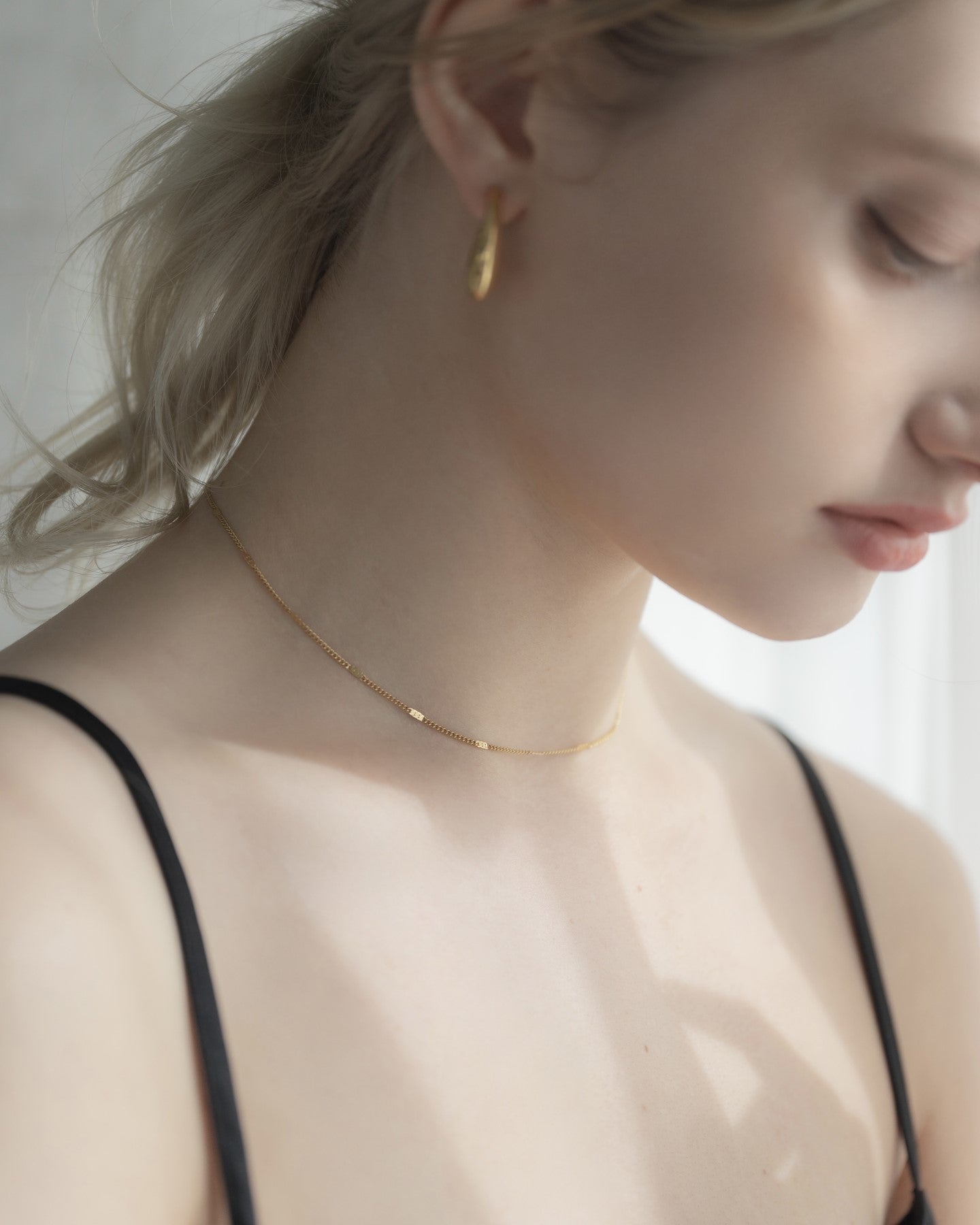 他のジュエリーと一緒にシンプルチェーンネックレスを着用する女性。重ね付けにも最適な、ミニマルでスタイリッシュなデザイン。