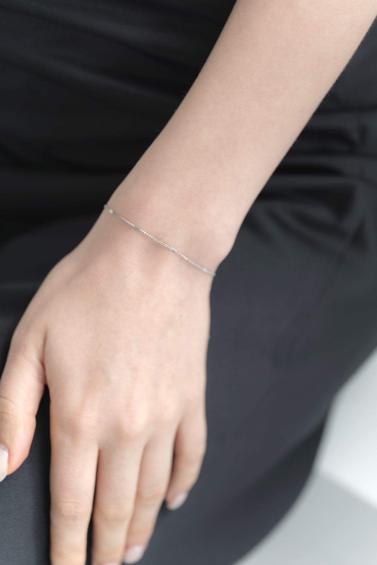 シンプルチェーンブレスレットを着用した女性の手首のクローズアップ。洗練されたデザインのステンレス製ブレスレットが手元を美しく飾る。