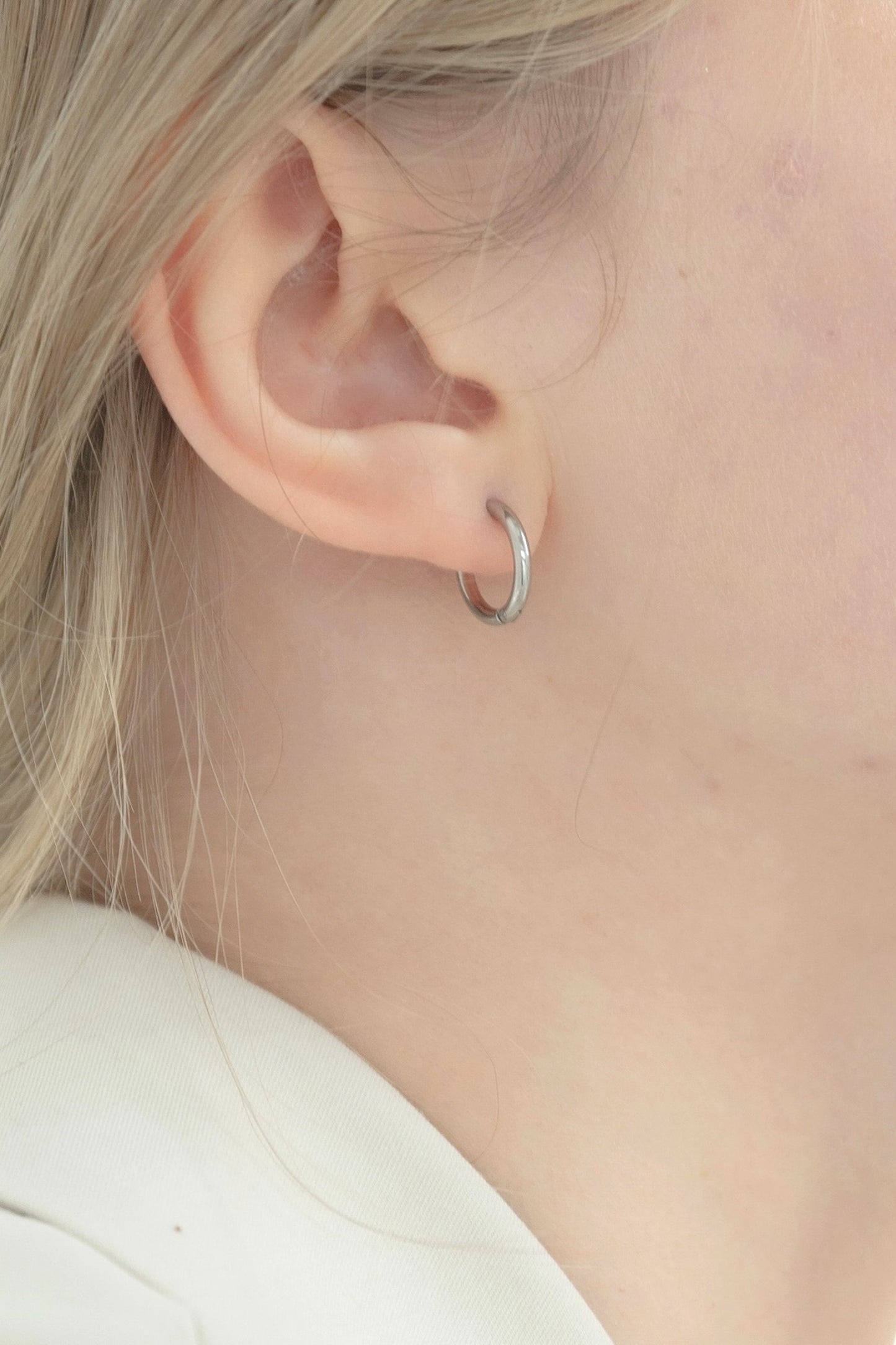シンプルフープピアスを着用した女性の耳元のクローズアップ。ステンレス製で洗練されたデザインのピアス。